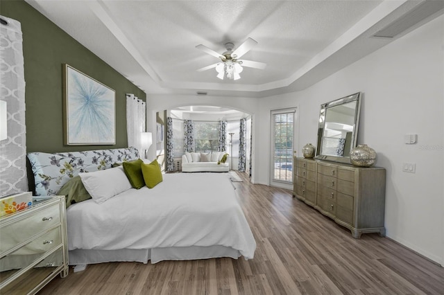 bedroom featuring visible vents, a tray ceiling, wood finished floors, arched walkways, and ceiling fan