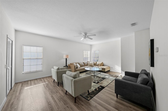 living area with visible vents, a ceiling fan, a textured ceiling, wood finished floors, and baseboards