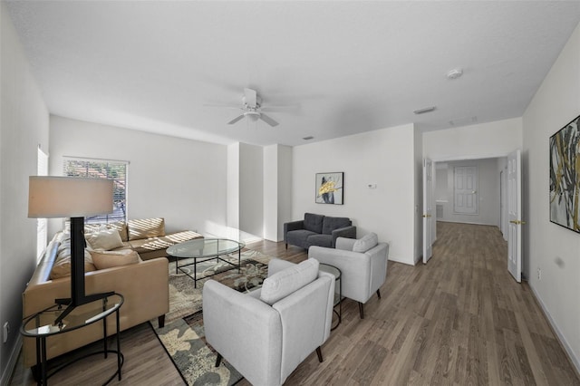 living room featuring ceiling fan, visible vents, baseboards, and wood finished floors