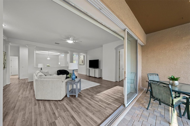 living area with decorative columns, light wood-style floors, baseboards, and ceiling fan