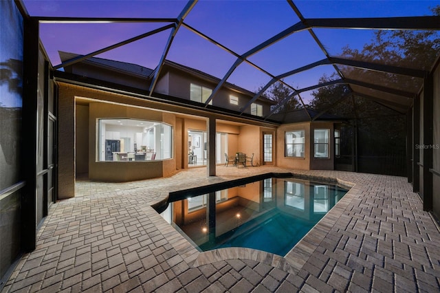 pool at dusk with glass enclosure, a patio area, and an outdoor pool