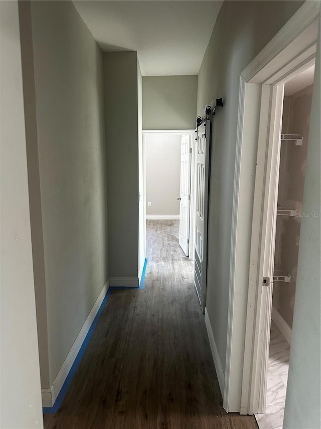 corridor featuring wood finished floors, baseboards, and a barn door