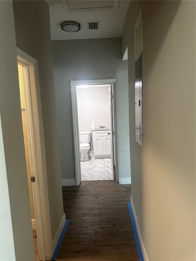 hall with a sink, wood finished floors, visible vents, and baseboards