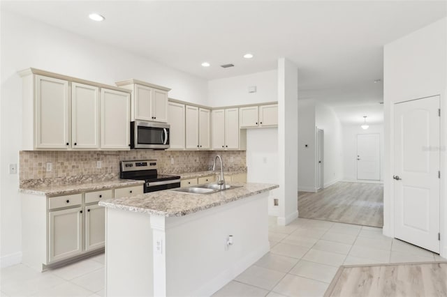 kitchen featuring light tile patterned floors, backsplash, appliances with stainless steel finishes, a sink, and an island with sink