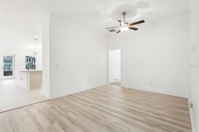 spare room with ceiling fan with notable chandelier, baseboards, a sink, and light wood-style floors