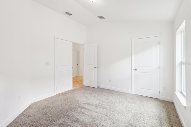 unfurnished bedroom with lofted ceiling, visible vents, baseboards, and light colored carpet