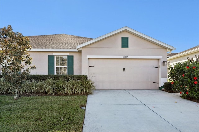 single story home featuring an attached garage, a shingled roof, concrete driveway, stucco siding, and a front yard