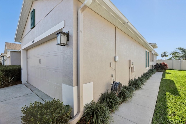 view of side of home with driveway, fence, a lawn, and stucco siding