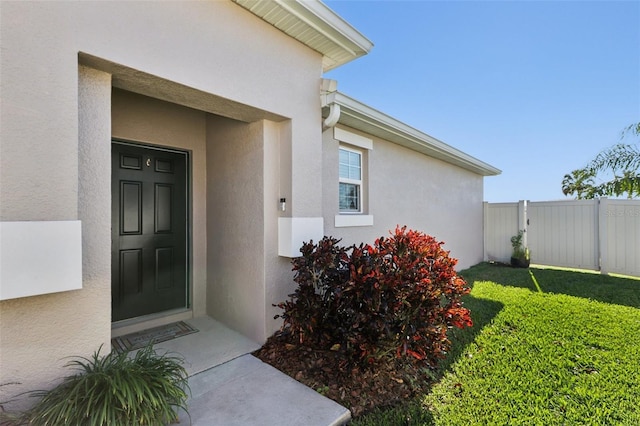 view of exterior entry featuring a yard, stucco siding, and fence