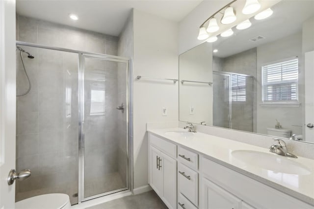 bathroom featuring a shower stall, double vanity, a sink, and toilet