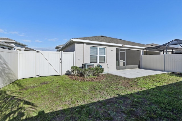 rear view of house with stucco siding, a lawn, a patio area, fence, and a gate