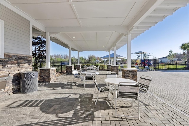 view of patio with outdoor dining space, fence, and playground community