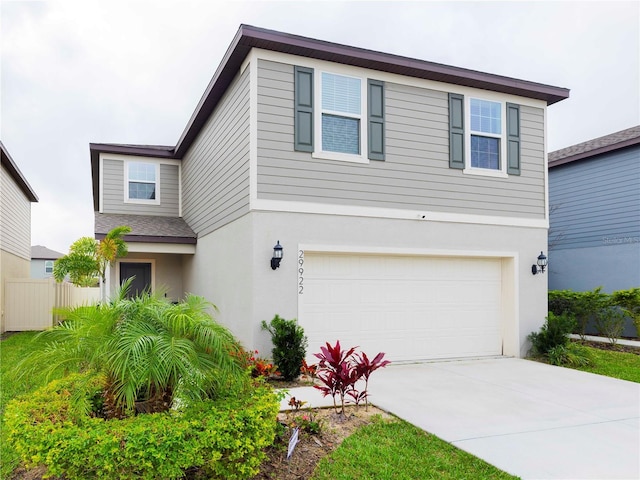 traditional-style home featuring a garage, concrete driveway, fence, and stucco siding