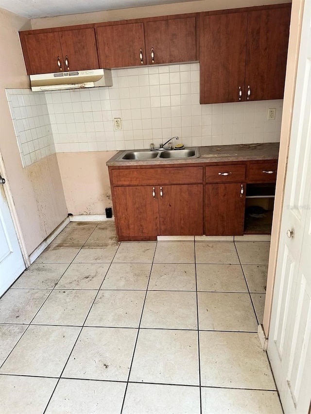 kitchen featuring light tile patterned flooring, under cabinet range hood, a sink, backsplash, and brown cabinets