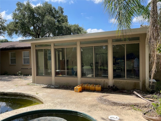 rear view of house featuring an in ground hot tub, a sunroom, and stucco siding