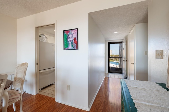 hall with a textured ceiling, baseboards, and wood finished floors