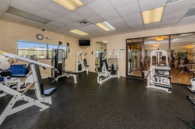 exercise room with visible vents, a paneled ceiling, and baseboards