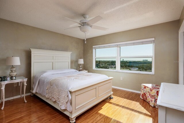 bedroom with a ceiling fan, light wood-style floors, baseboards, and a textured ceiling