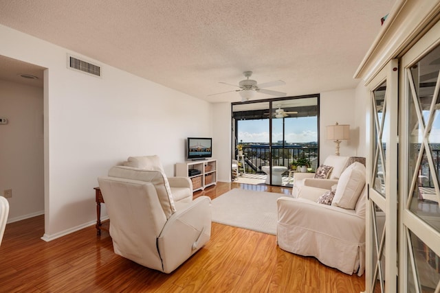 living room featuring visible vents, baseboards, a textured ceiling, and wood finished floors