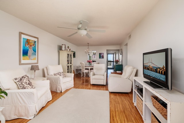 living room featuring ceiling fan with notable chandelier, visible vents, and light wood finished floors