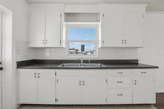 kitchen featuring dark countertops, a sink, white cabinetry, and decorative backsplash