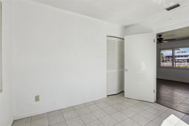 empty room featuring light tile patterned floors, visible vents, baseboards, ceiling fan, and ornamental molding