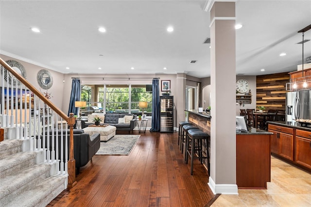 living area with ornate columns, stairs, crown molding, light wood-style floors, and recessed lighting