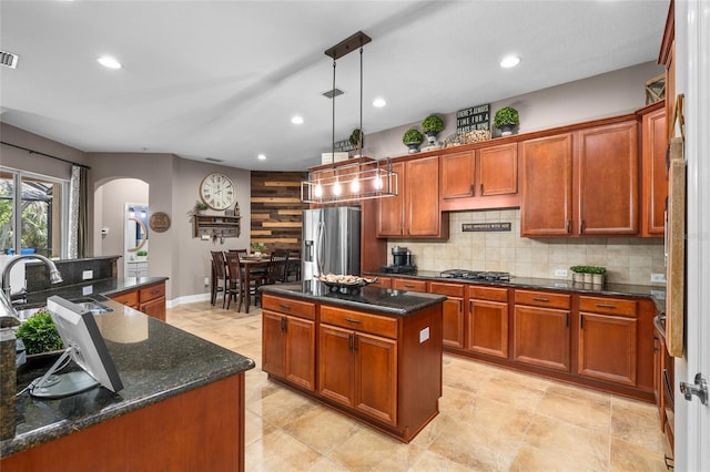 kitchen featuring arched walkways, tasteful backsplash, appliances with stainless steel finishes, a kitchen island, and a sink