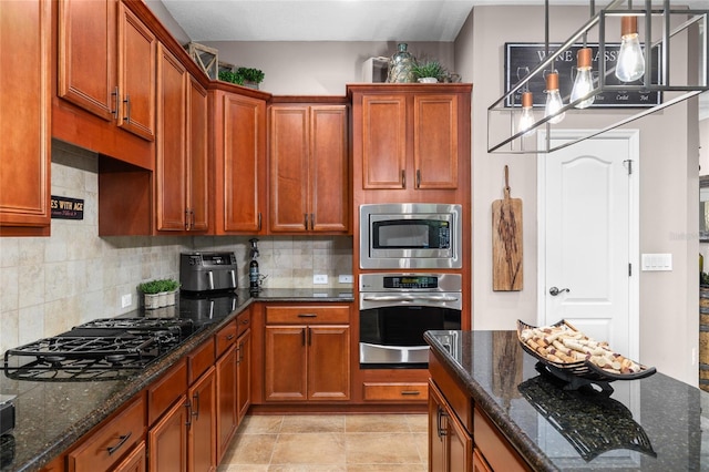 kitchen featuring appliances with stainless steel finishes, dark stone counters, brown cabinets, and tasteful backsplash