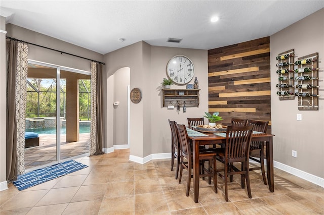 dining room with arched walkways, a textured ceiling, an accent wall, wood walls, and visible vents