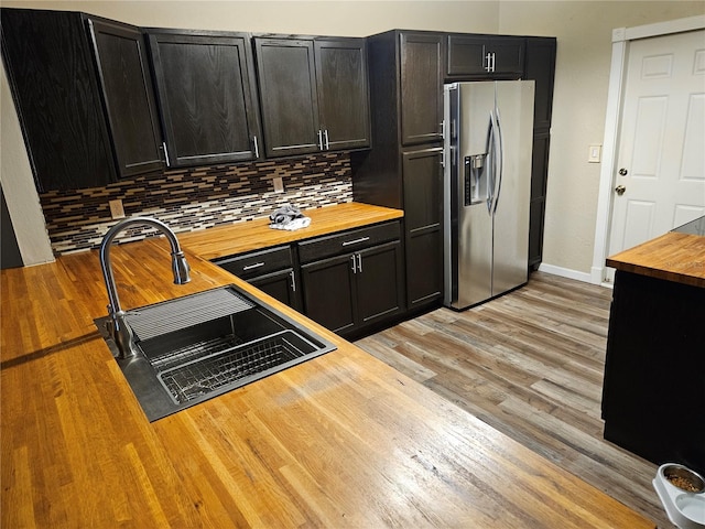 kitchen featuring butcher block countertops, dark cabinetry, light wood-style flooring, and stainless steel refrigerator with ice dispenser