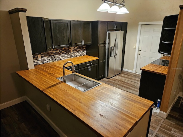 kitchen with stainless steel refrigerator with ice dispenser, wooden counters, backsplash, a sink, and wood finished floors