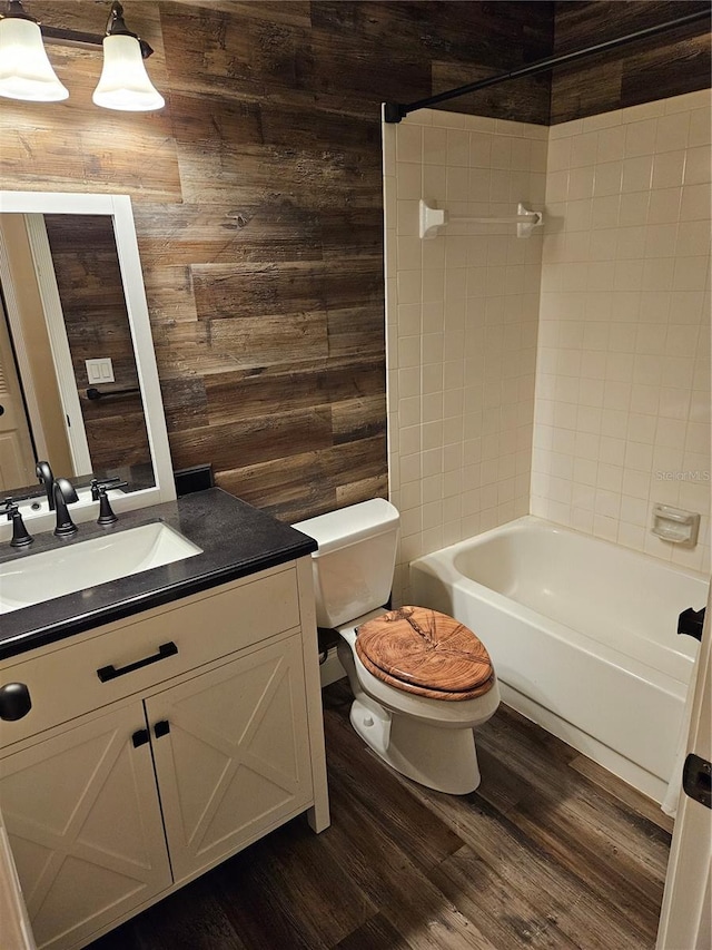 full bath with shower / bathtub combination, toilet, wooden walls, wood finished floors, and vanity