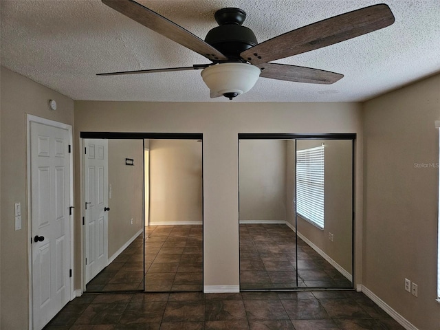 unfurnished bedroom with multiple closets, a textured ceiling, baseboards, and a ceiling fan