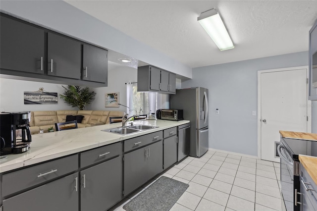 kitchen with light tile patterned floors, stainless steel appliances, gray cabinetry, a sink, and a textured ceiling