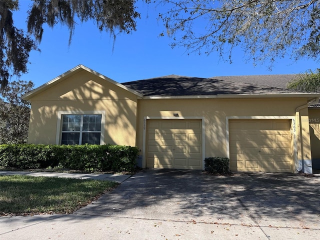 single story home with a garage, driveway, a shingled roof, and stucco siding