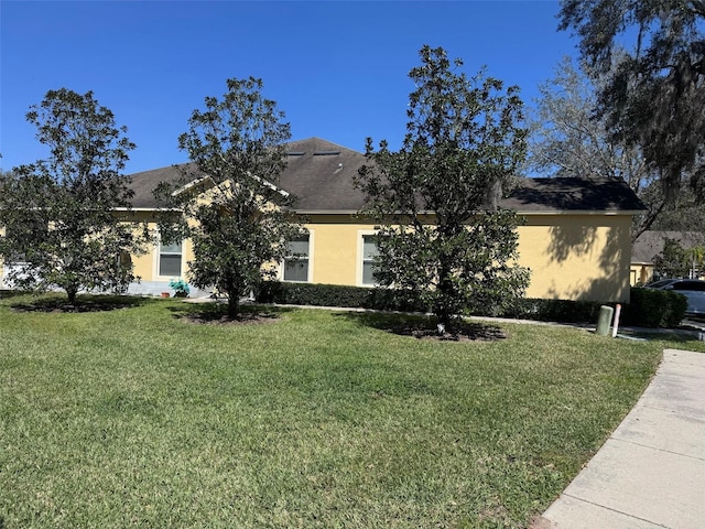 view of front of home with a shingled roof, a front yard, and stucco siding