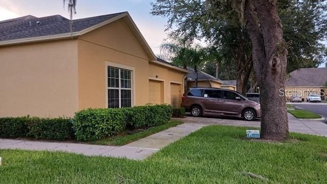 view of property exterior with a garage, concrete driveway, a lawn, and stucco siding