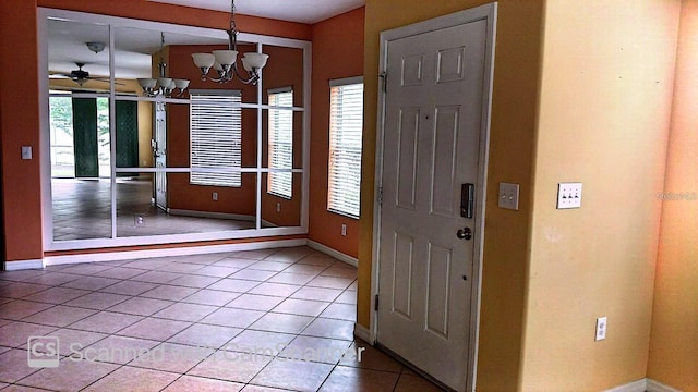 tiled foyer entrance featuring baseboards and ceiling fan with notable chandelier