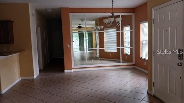 unfurnished dining area with tile patterned flooring, a notable chandelier, and baseboards