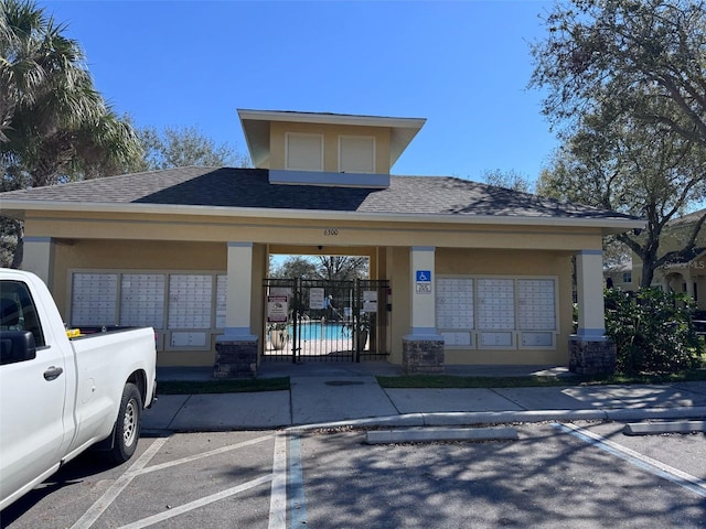 view of front facade with a shingled roof, uncovered parking, fence, and stucco siding