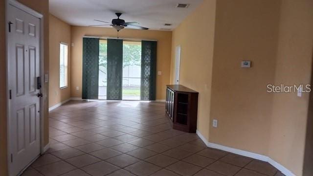 tiled empty room featuring baseboards, visible vents, and ceiling fan