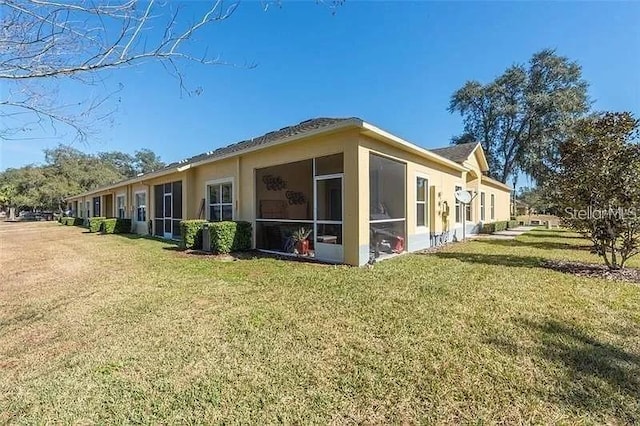 rear view of house featuring a sunroom, a lawn, and stucco siding