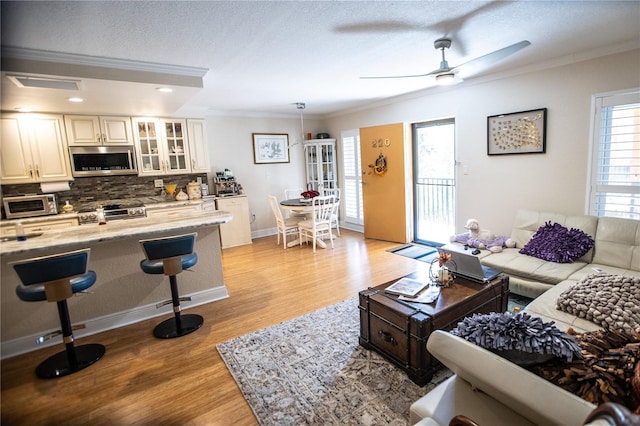 living room featuring ornamental molding, baseboards, a textured ceiling, and light wood finished floors