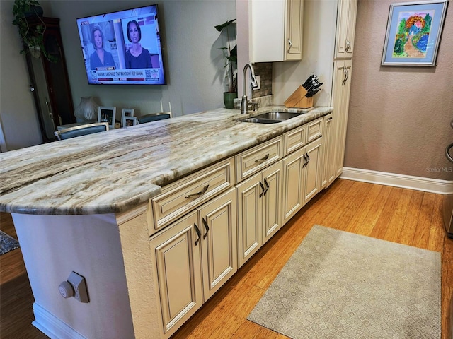 kitchen featuring light wood-style floors, cream cabinetry, a sink, and a peninsula