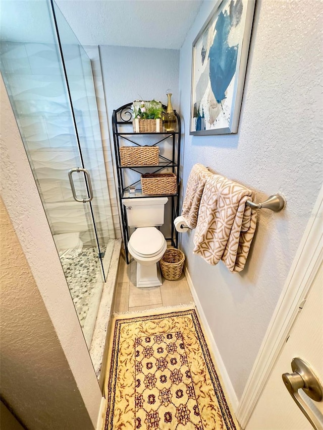 full bathroom featuring a textured wall, a shower stall, toilet, and baseboards