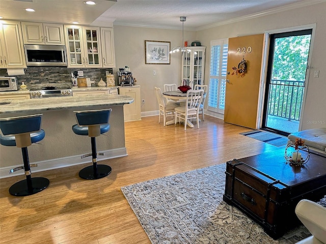 kitchen with light wood-style floors, appliances with stainless steel finishes, tasteful backsplash, a kitchen bar, and crown molding