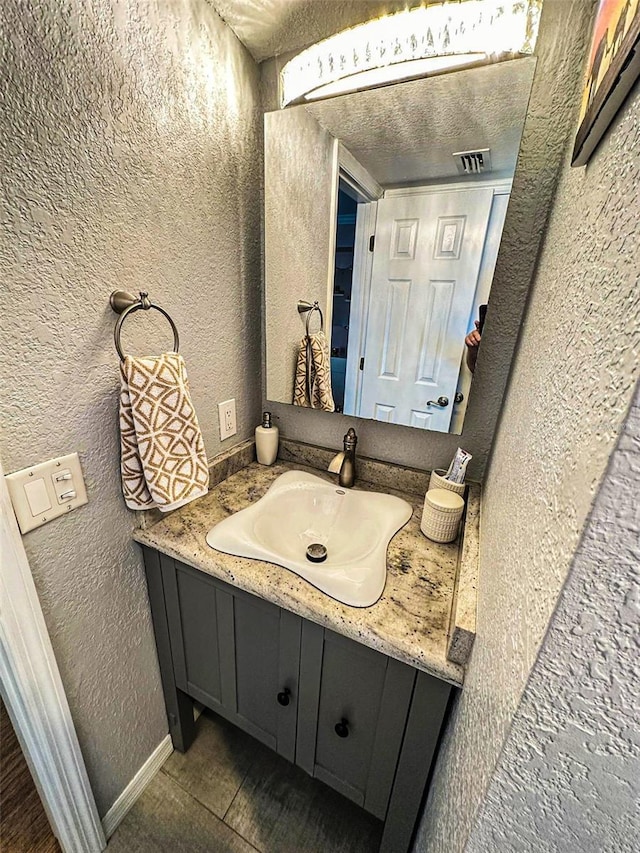 bathroom featuring visible vents, a textured wall, vanity, a textured ceiling, and baseboards