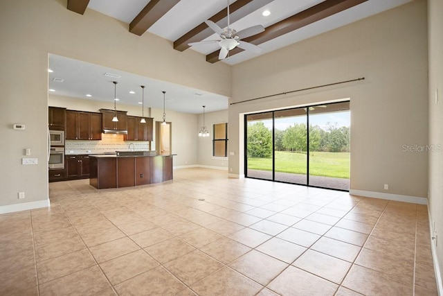 kitchen featuring beam ceiling, under cabinet range hood, tasteful backsplash, open floor plan, and stainless steel appliances