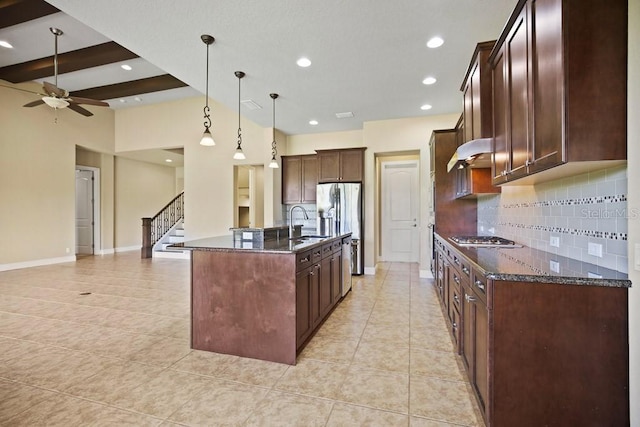 kitchen featuring dark stone counters, a ceiling fan, under cabinet range hood, and a sink